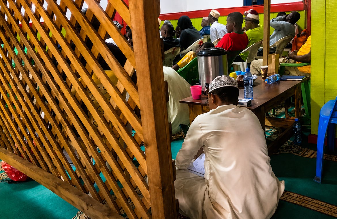 Men seated for a lesson beside a wooden screen